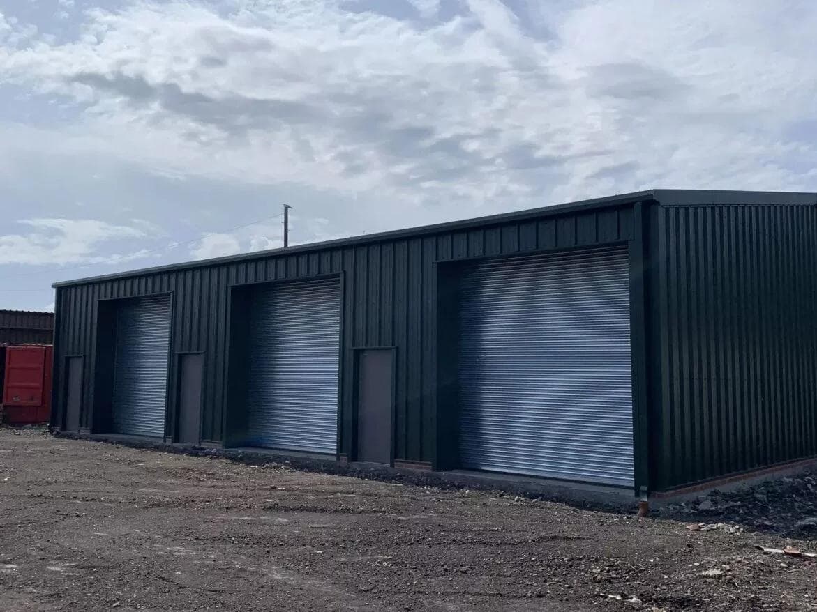 Steel-framed storage units with roller shutter doors, dark cladding and brick plinth